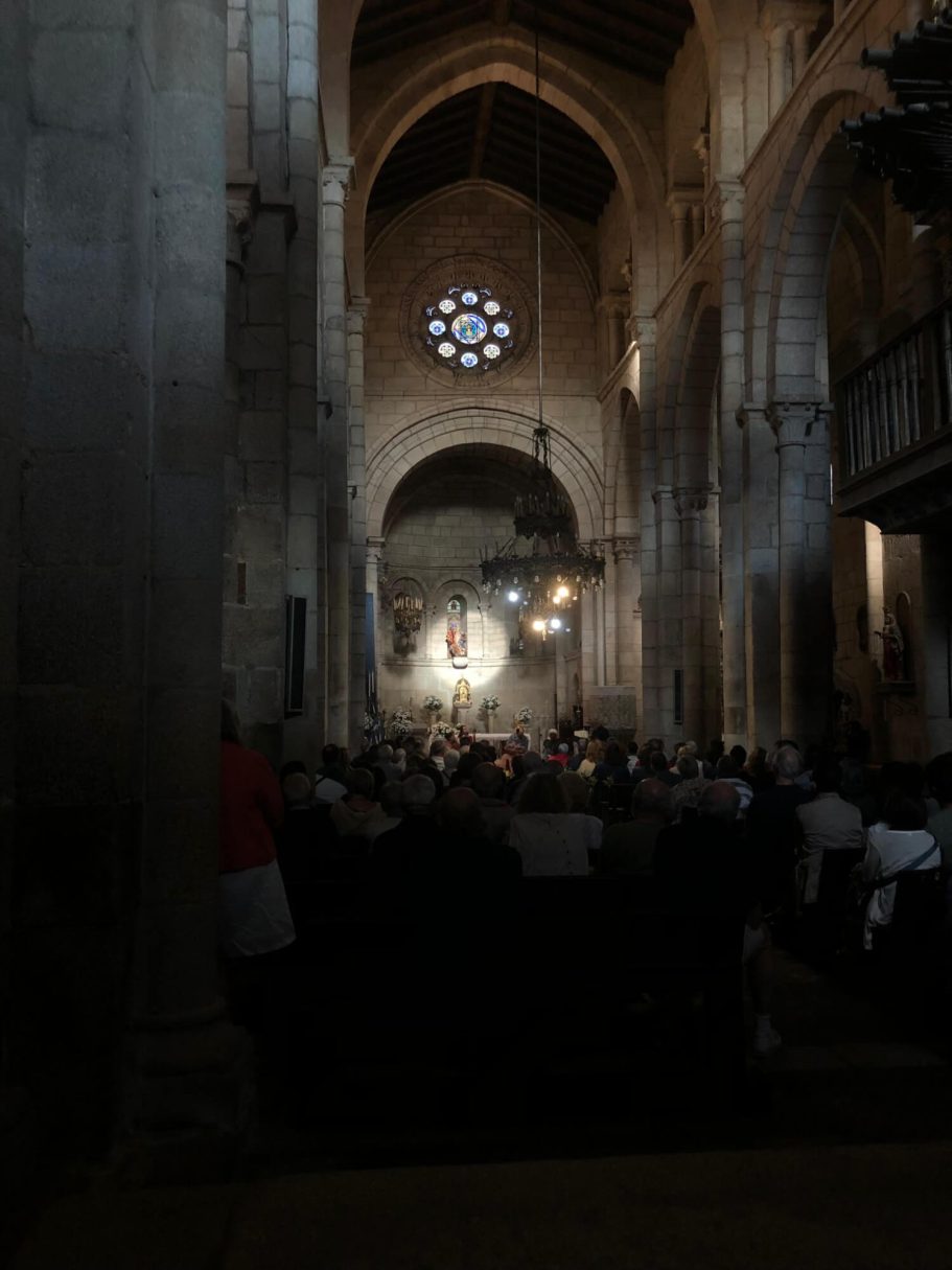 Nave central Vista interior da nave central da igrexa cara ao altar, con arcos de pedra e bancos de madeira ás escuras.