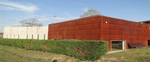 Edificio moderno de cor avermellada e deseño contemporáneo que funciona como albergue, situado nunha contorna verde.