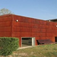 Edificio moderno de cor avermellada e deseño contemporáneo que funciona como albergue, situado nunha contorna verde.