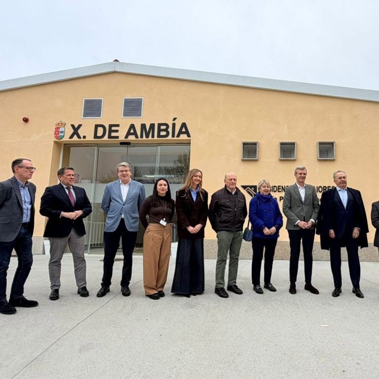 Fachada simétrica dun edificio moderno dunha soa planta con paredes de cor salmón, zona central acristalada e dúas árbores a cada lado.