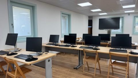  Sala de informática luminosa equipada con varias mesas de madeira e ordenadores de sobremesa aliñados e listos para o seu uso.
