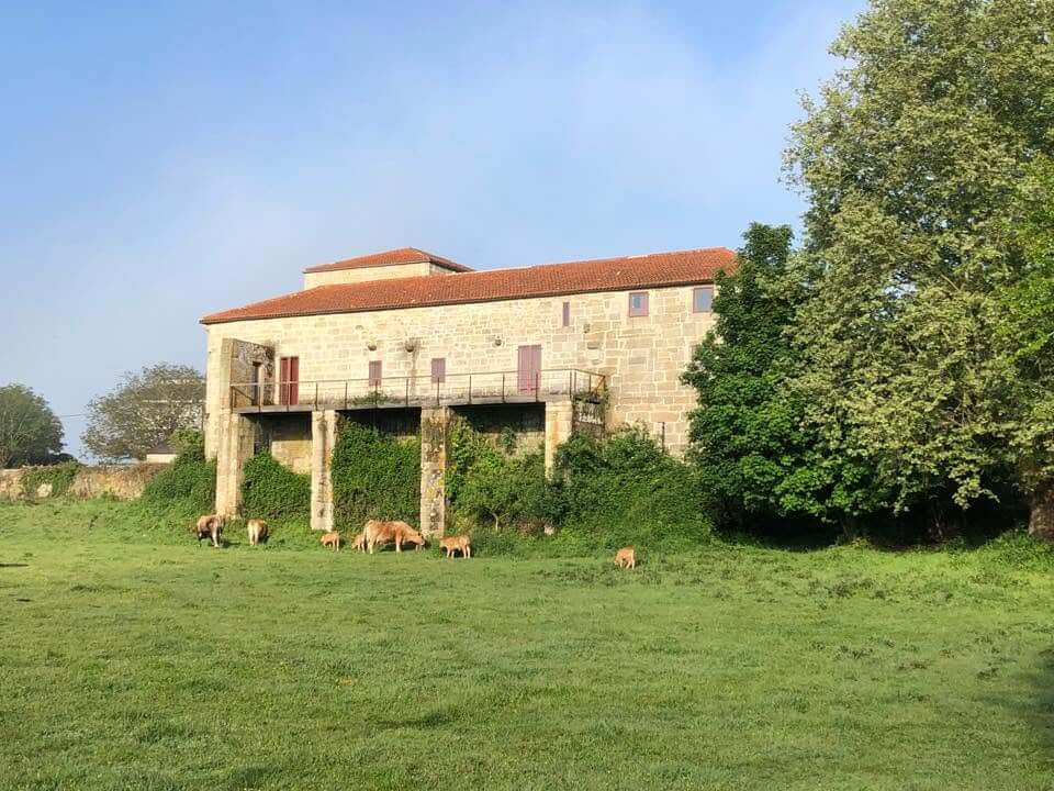 O Pazo Prioral Edificio histórico situado nun prado verde, con muros de pedra na planta baixa e unha fachada branca na planta superior.