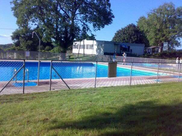 Piscinas Vista de dúas piscinas ao aire libre rodeadas de céspede verde e árbores nun día asollado.
