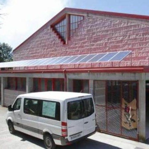 Fachada de ladrillo do polideportivo municipal, que conta con paneis solares no tellado e unha furgoneta branca aparcada diante da porta.
